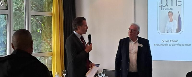 Dejeuner CPME 91 avec présentation sur l'écran en arrière plan, 1 homme avec micro et 1 autre homme debout à coté. L'audience est autour de table de déjeuner.