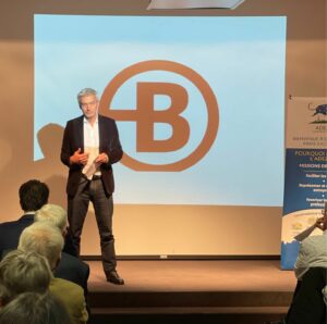 Présentation Nicolas Potier, dirigeant de Bruneau au Café Rencontre de l'ADEZAC. M. Potier debout sur scène devant l'assemblée. Logo Bruneau en arrière plan sur l'écran projecteur