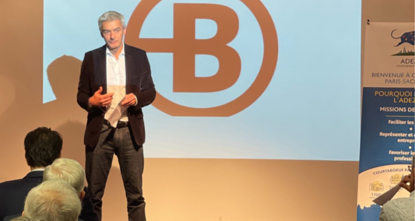 Intervention de Nicolas Potier au Café Rencontres de l'ADEZAC. Monsieur Potier sur scène, debout. En arrière plan logo Bruneau diffusé sur écran projecteur.