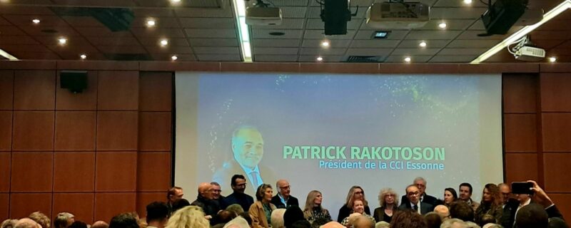 photo de la soirée des voeux de la CCI Essonne. Au premier plan l'assemblée assise. En arrière plan, les membres de la CCI et son président Patrick Rakotoson avec sa photo diffusée sur le rétro-projecteur à l'arrière.